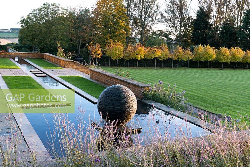 Long ruisseau de terrasse se terminant en piscine avec une pièce d'eau en sphère d'ardoise créée par le sculpteur James Parker.