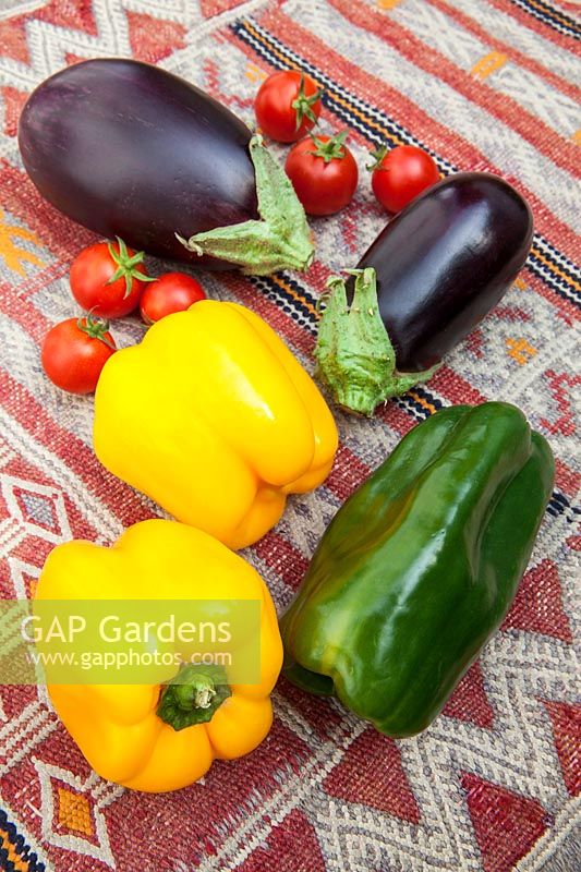 Légumes frais colorés - poivrons jaunes et verts avec aubergines et tomates cerises sur une table couverte de kilim