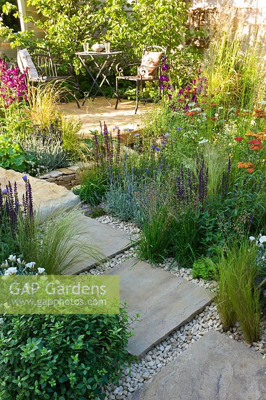 Petit jardin avec dallage en pierre sinueuse, chemin de gravier et coin salon, et parterres de fleurs et d'herbes