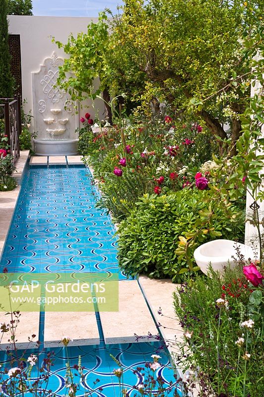 Un jardin exotique avec un large ruisseau d'eau et des parterres luxuriants de grenadiers et de roses