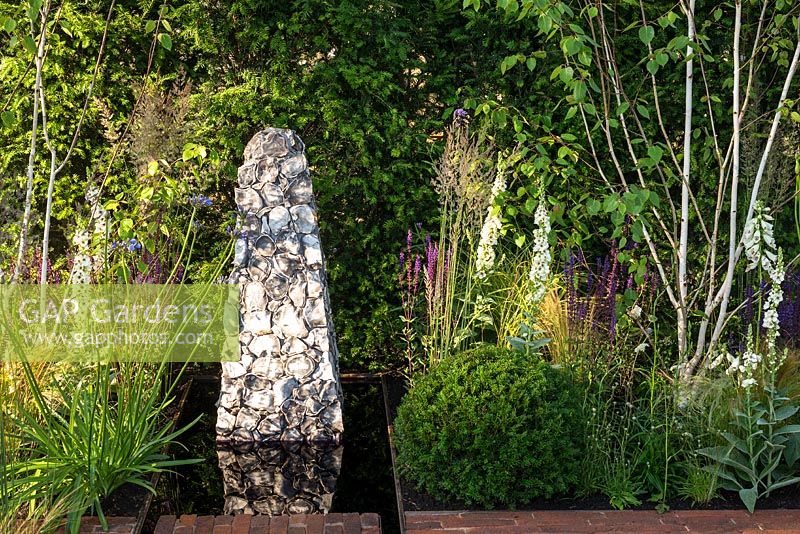 Jardin contemporain avec sculpture en pierre dans une piscine d'eau rectangulaire