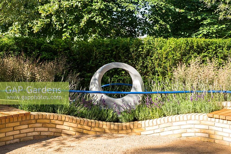 Sculpture circulaire et mur de briques de jardin incurvé avec garde-corps bleu et herbes. Designer Rae Wilkinson
