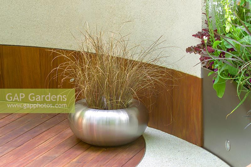 Le Chelsea Flower Show 2005, Londres, Royaume-Uni. 'Urban Space: Modern Eden' (Kate Gould) matériaux et textures mélangés, pot en métal avec plantation d'herbe, terrasse en bois et mur incurvé