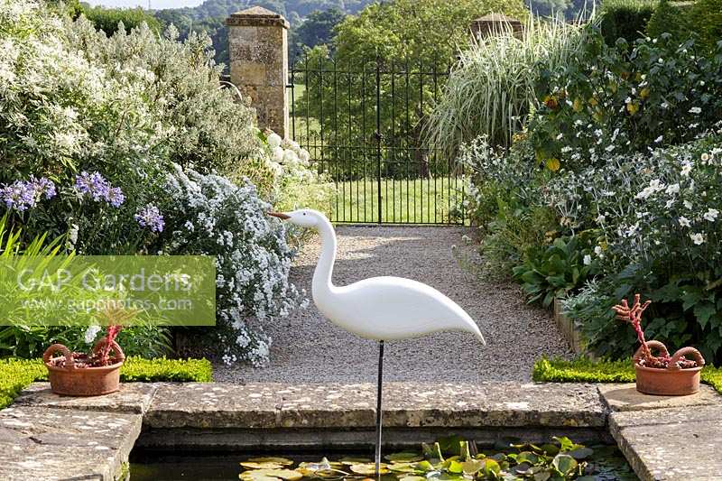 Bourton House Garden, Gloucestershire. Mi-été. Héron par Michael Lythgoe, sculpture d'oiseau dans un étang formel