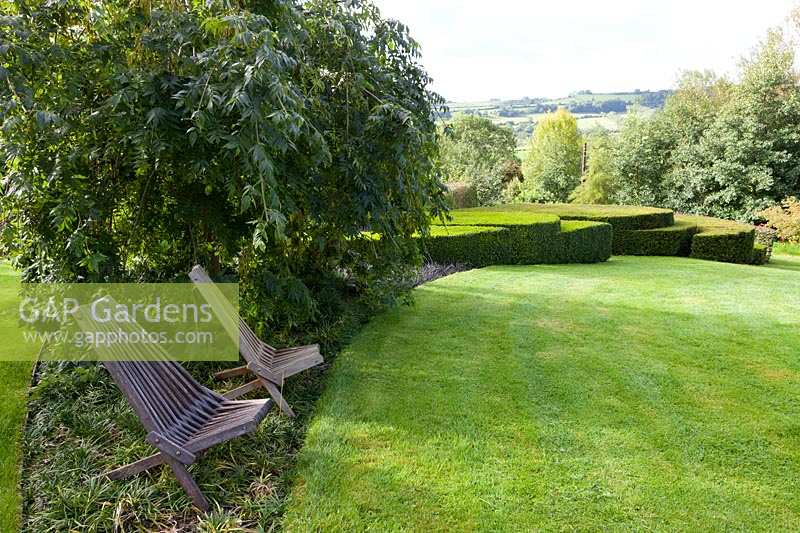 Derry Watkins Garden at Special Plants, Bath, Royaume-Uni. Transats en bois au bord d'une pelouse circulaire en forme