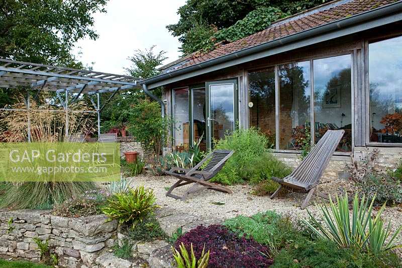 Jardin Derry Watkins à Special Plants, Bath, Royaume-Uni, bâtiment 'architectural' moderne avec terrasse et transats en bois