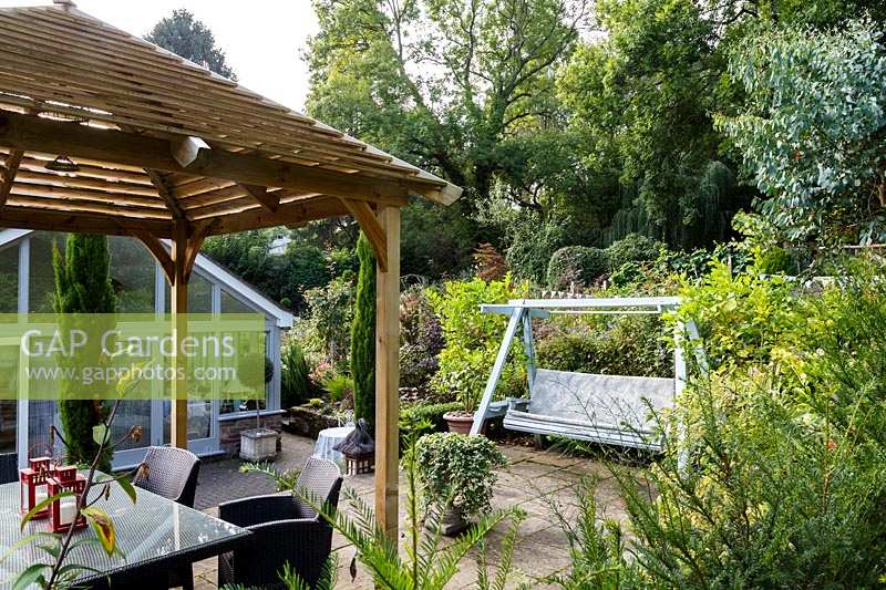 Le jardin de Jackie Healy près de Chepstow. Jardin au début de l'automne. 'Pergola' en bois de style japonais et banc de balançoire dans le patio