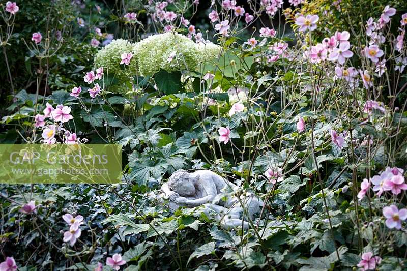 Le jardin de Jackie Healy près de Chepstow. Jardin au début de l'automne. Statue 'endormie' chez Anemone x hupehensis