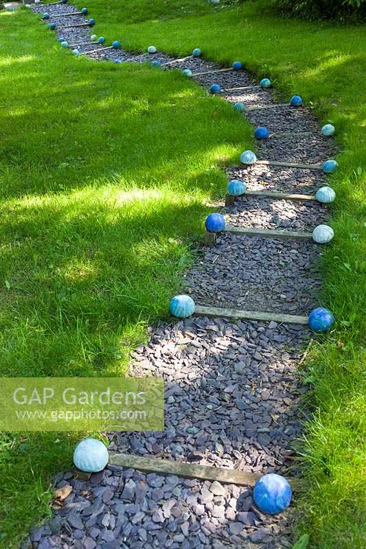 Jardin de Carole Waller à Bathford, Somerset, l'été. Des sphères décoratives marquent le chemin escarpé dans le jardin