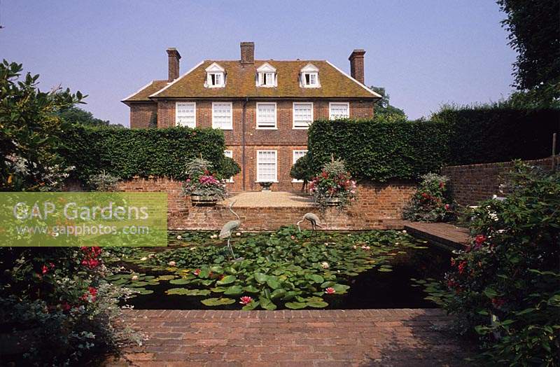 Le Manor House Bledlow Buckinghamshire étang de nénuphar formel coulé avec des statues de grue pavage de briques chemin de gravier haies d'ifs