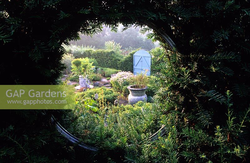 Tilford Cottage Surrey Vue du jardin d'herbes formelles à travers une fenêtre circulaire en if if