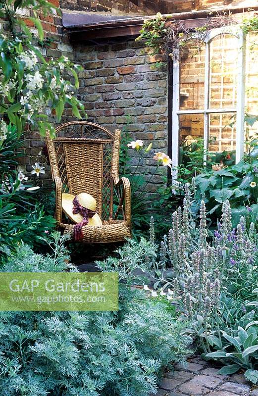 Chaise en rotin avec chapeau de paille dans un coin d'un petit jardin clos