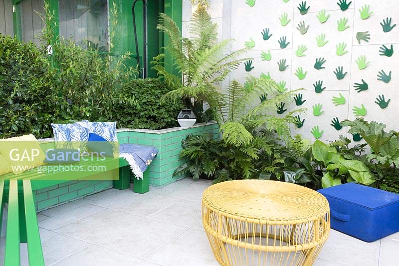 Espace de vie moderne et coloré avec bancs, tables et plantation de feuillage. Conçu par Kate Gould Gardens, parrainé par Greenfingers Charity, RHS Chelsea Flower Show, 2019.
