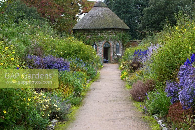 Un chemin vers un pavillon de chaume bordé de vivaces à floraison tardive, West Dean Gardens, Chichester