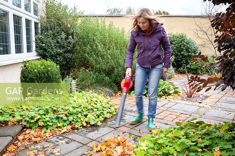 Femme à l'aide d'un souffleur de feuilles pour ramasser les feuilles d'un patio.