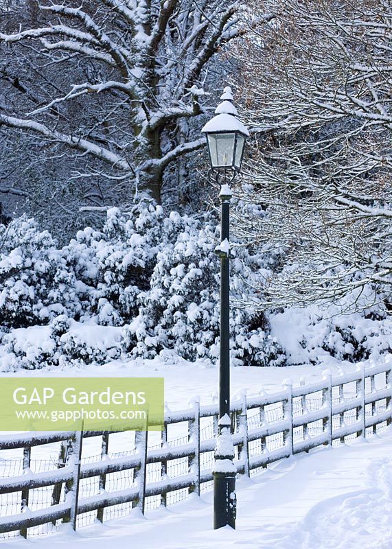 Jardin avant avec lampe à gaz ornementale et clôture de jardin dans la neige.