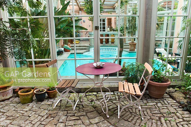 Une table et des chaises de bistrot sont installées devant la piscine intérieure. Marina Wüst garden, Allemagne.
