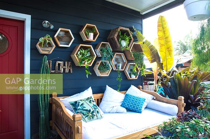 Méridienne de style balinais sur une véranda devant un mur de jardinières hexagonales en bois.