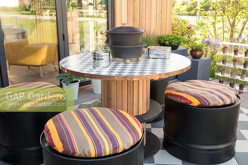 Table en bois recyclée avec sièges et coussins pour fûts d'huile. Jardin «À la maison - grandir, dîner, se détendre», RHS Malvern Spring Festival, 2018.