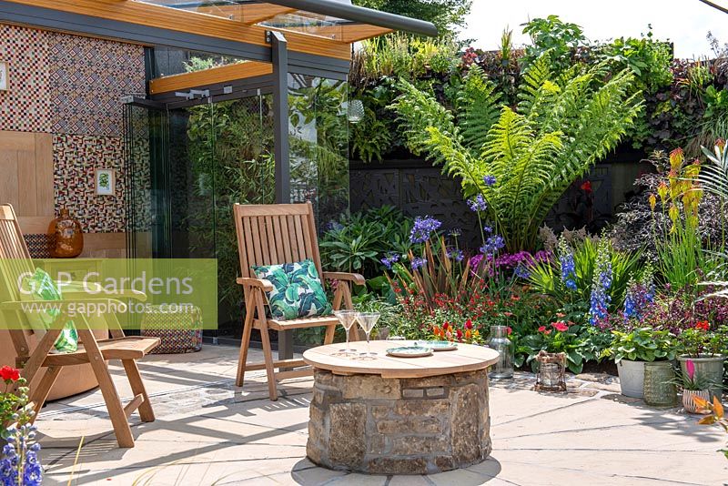 Chaises en bois et table circulaire dans un jardin exotique moderne. 'Jungle Fever', RHS Tatton Park Flower Show, 2018.