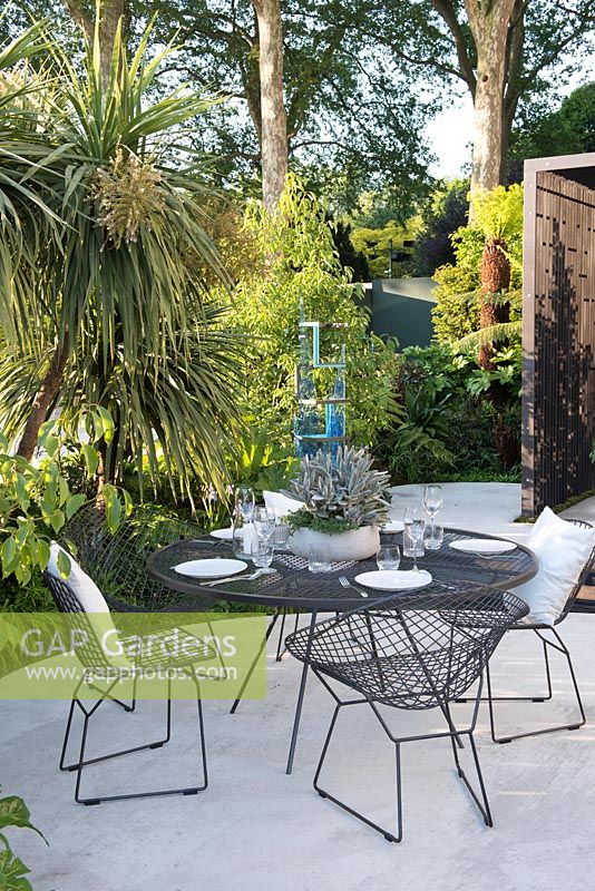 Cordyline australis avec table et chaises en métal. VTB Capital Garden - Spirit of Cornwall, RHS Chelsea Flower Show, 2018. Commanditaire: VTB Capital