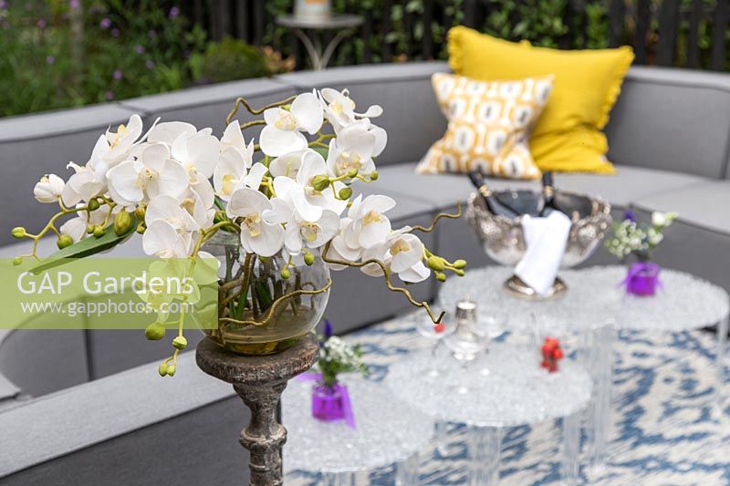 Arrangement floral d'orchidée, avec vue sur l'arrangement de canapé extérieur gris et les tables en verre.