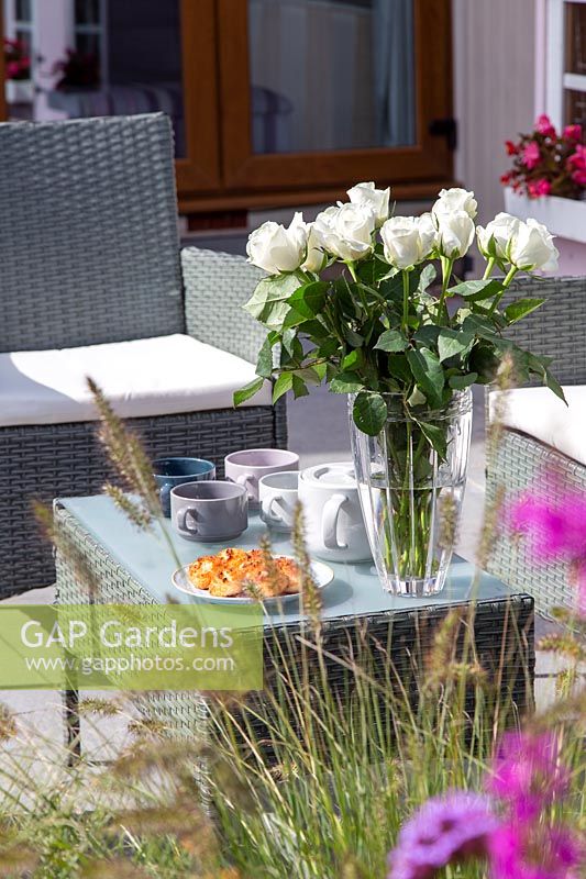Meubles de salon sur patio - ensemble pour le thé de l'après-midi avec des tasses, des gâteaux et des compositions florales.