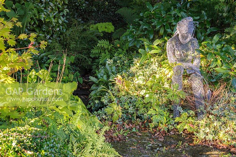 Sculpture de figure féminine assise par Derek Kinzett entouré de plantes à feuillage - Shropshire, Royaume-Uni
