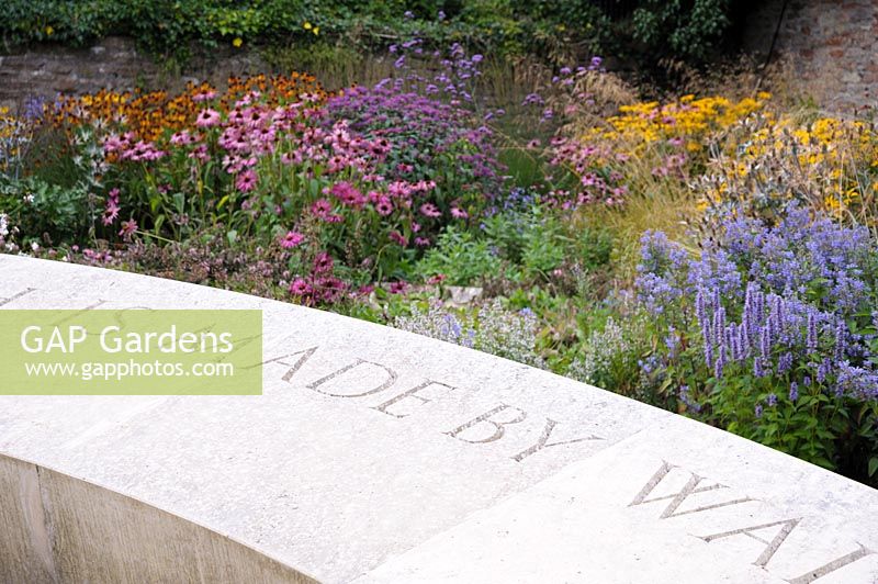 Le parterre de fleurs de la fin de l'été derrière un vaste siège en pierre de 40 'est planté d'échinacées, de Verbena bonariensis, d'agastaches, d'héléniums et d'herbes dans le jardin de réflexion du Bishop's Palace Garden, Wells