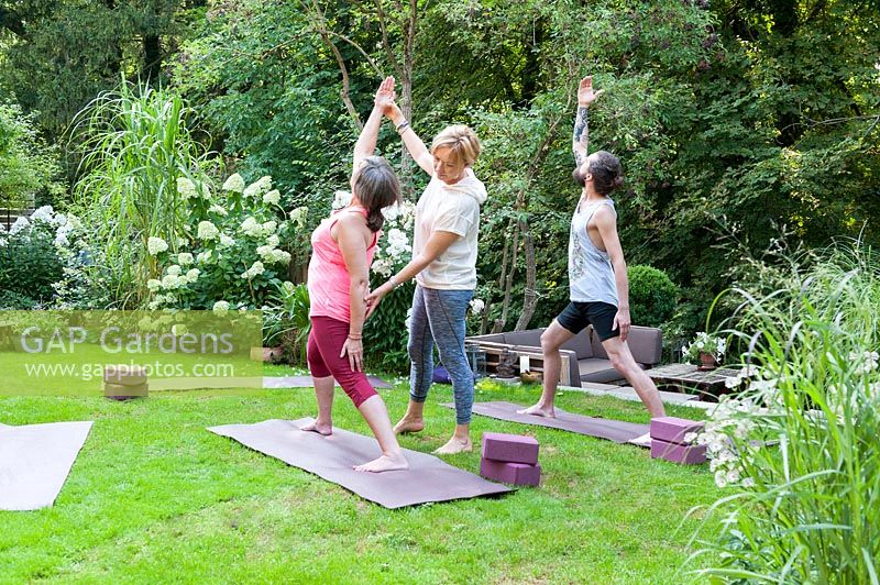 Cours de yoga dans un jardin verdoyant. L'enseignant corrige la position appelée Virabhadrasana