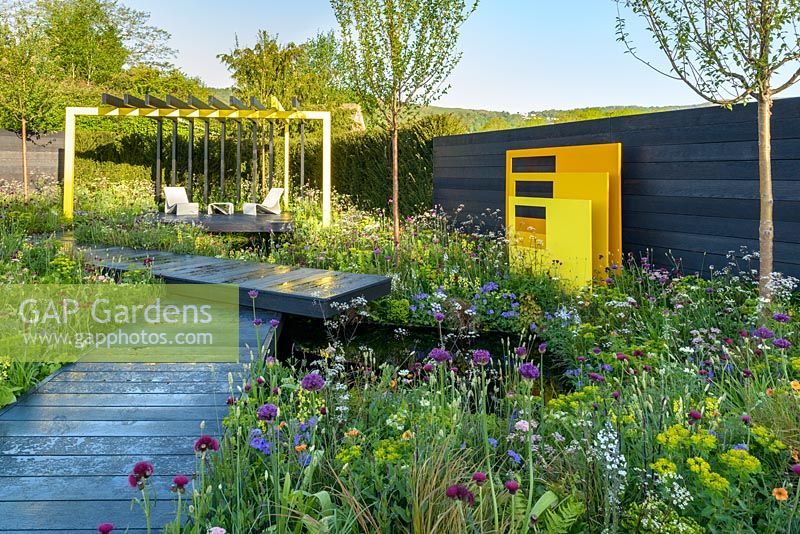Panneaux sculpturaux en acier jaune avec fond de clôture noire dans une plantation de style pré - 'Urban Oasis', RHS Malvern Spring Festival 2018, parrainé par Graduate Gardeners Ltd.