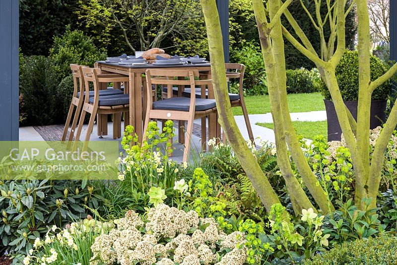 Vue sur la plantation mixte de la salle à manger avec table et chaises en bois - Jardin 'The Landform Spring' - Ascot Spring Garden Show, 2018.