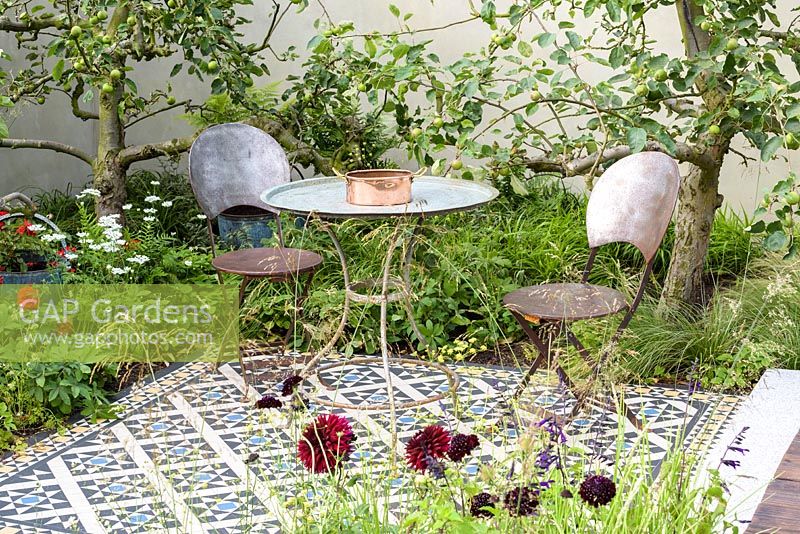 Table et chaises sur terrasse carrelée de mosaïque. 'Style and Design Garden', RHS Hampton Flower Show 2018