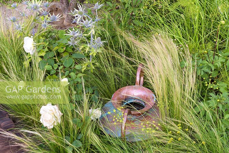 Roses blanches, Stipa et Eryngium avec cruche en cuivre. 'Style and Design Garden', RHS Hampton Flower Show 2018