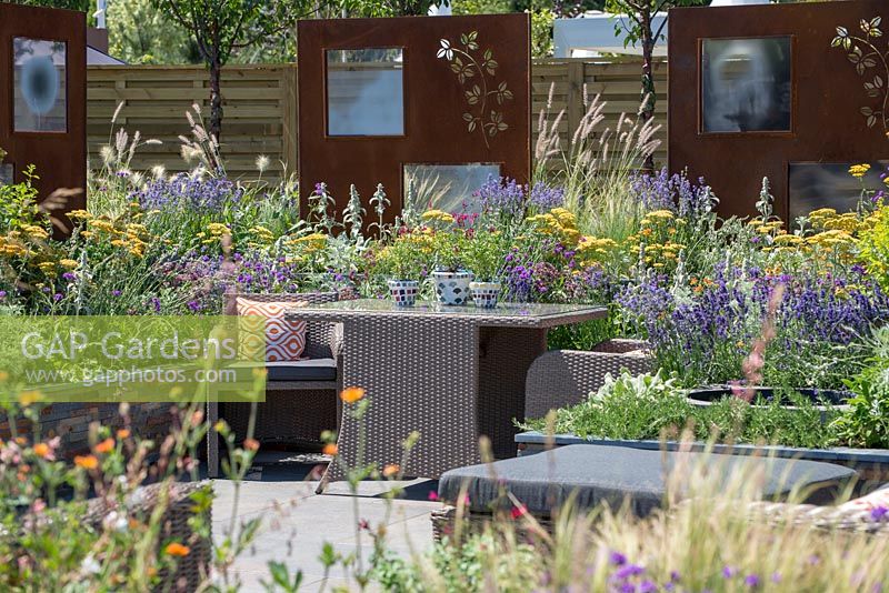 Mobilier de salle à manger en rotin extérieur entouré de plantes colorées - RNIB's Community Garden, RHS Hampton Court Palace Flower Show 2018