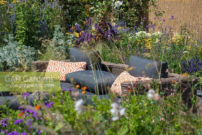 Canapé en rotin extérieur entouré d'un parterre de fleurs surélevé avec une plantation de plantes vivaces mixtes - RNIB's Community Garden, RHS Hampton Court Palace Flower Show 2018