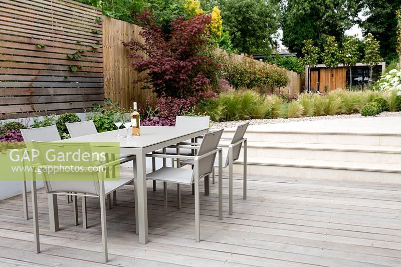 Table de jardin contemporaine sur terrasse en bois, avec vue sur les marches menant à la partie principale du jardin. Jardin contemporain à Dulwich