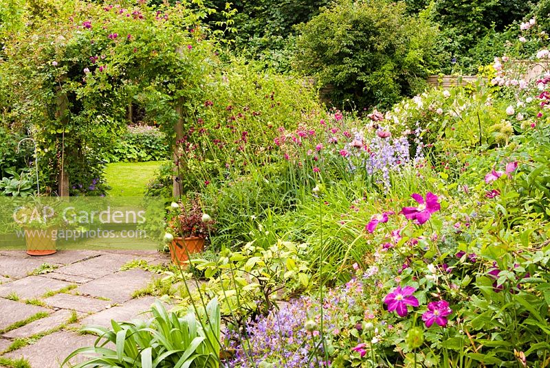 Vue le long du jardin vivace en fleurs à l'arche couverte de roses.