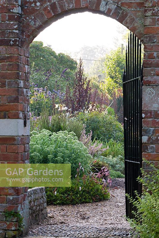 Vue à travers la porte dans le jardin clos et le long de parterres de plantes herbacées doubles à Edmondsham House, Cranborne, Wimborne Minster, Dorset, UK