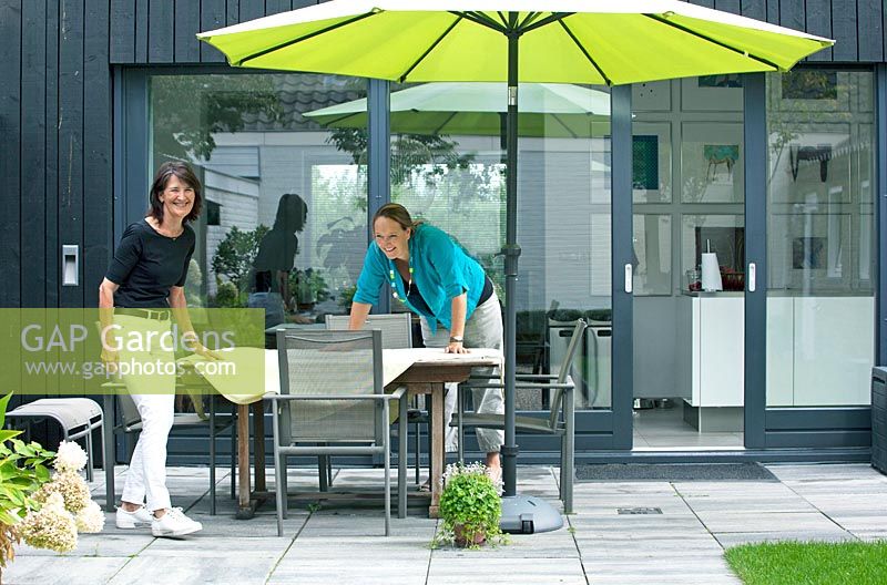 Deux femmes installant une table sur la terrasse du jardin.