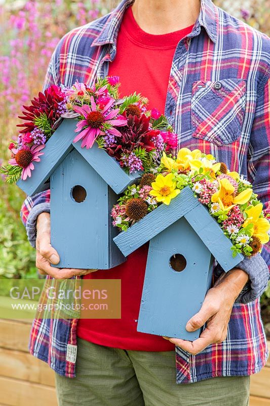Personne tenant une paire de nichoirs en bois avec des toits ornés de fleurs