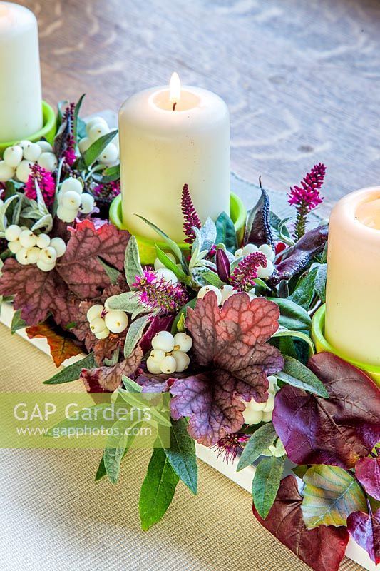 Arrangement de bougies d'automne avec Heuchera, feuilles de Buddleja, fleurs de Hebe, gousses de Lablab purpureus et Symphoricarpos - snowberry.