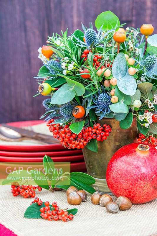 Vue de l'arrangement floral festif terminé sur la table, avec des grenades, des noisettes et de la vaisselle.