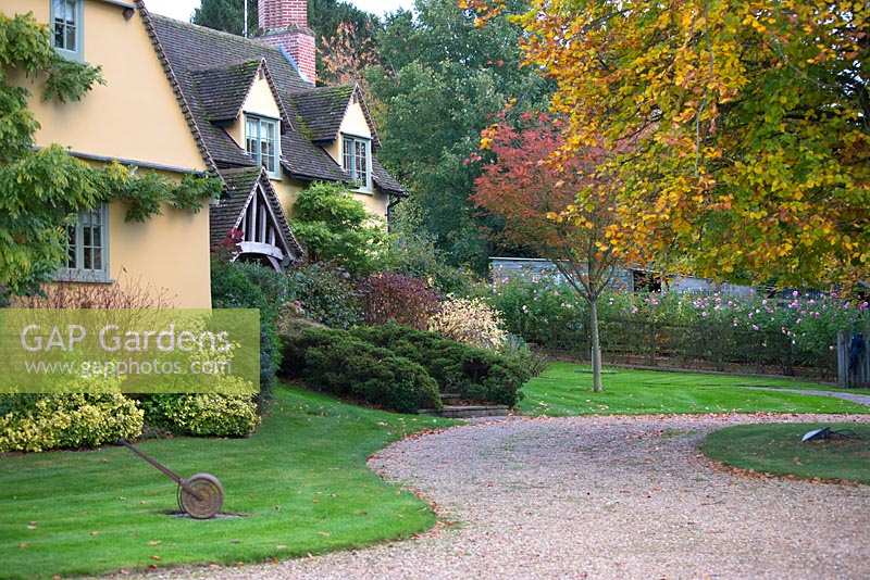 Entrée de la maison avec grande route et arbustes et arbres automnaux.