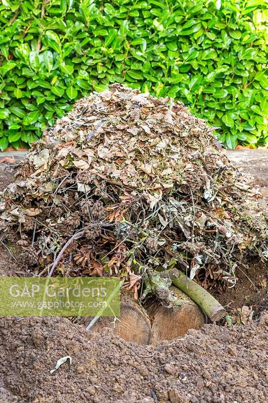 Creuser une tranchée dans un parterre de fleurs vide, rempli de branches d'arbres et de bûches, de déchets de jardin et de feuilles, dans le cadre de la méthode Hugelkultur.