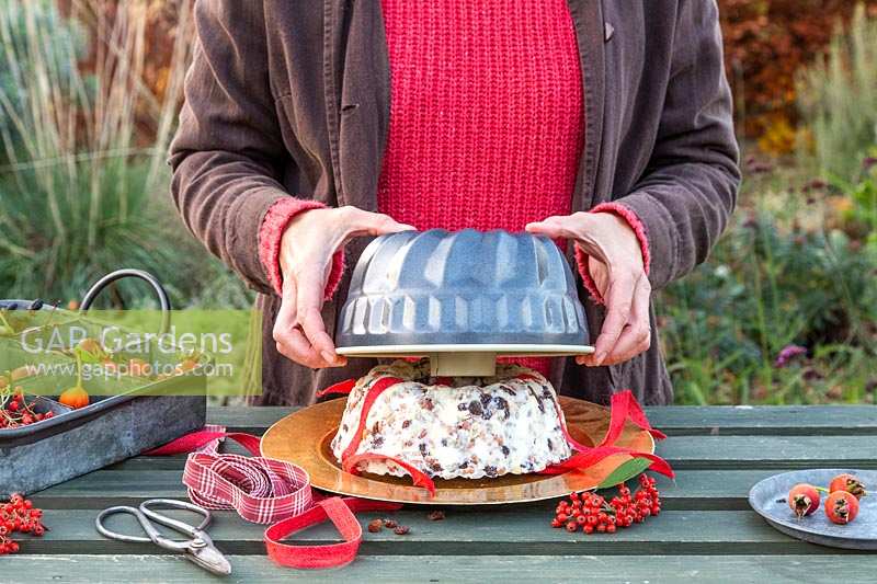 Femme levant le moule à cake bundt pour révéler le gâteau bundt pour oiseaux, à base de saindoux, de raisins secs et de noix.