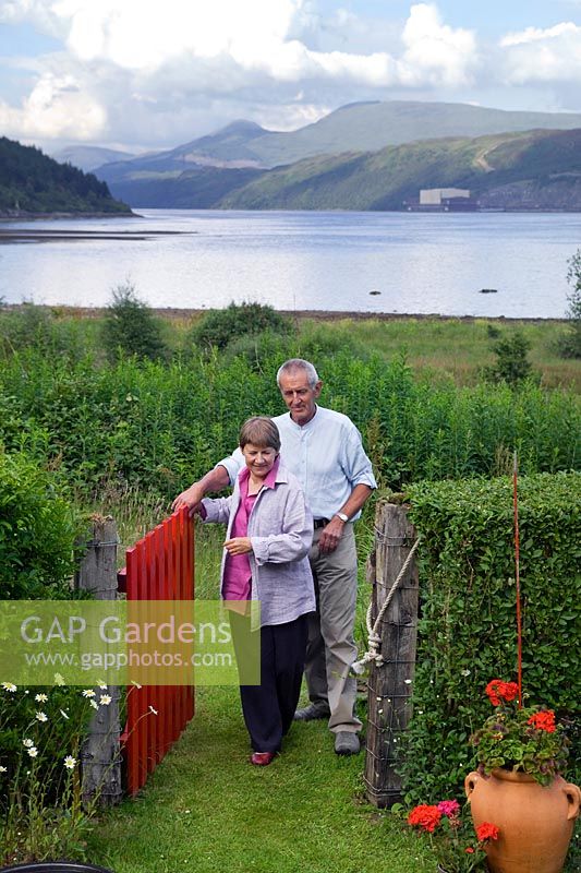 Freda et Barry Waldapfel entrent dans le jardin arrière par la porte du rivage. Loch Long, Dunoon, Ecosse, Royaume-Uni.