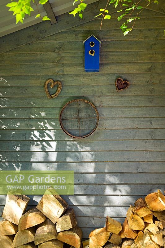 Magasin de rondins à l'arrière de la maison d'été avec nichoir, cœurs de saule tissés et vieux tamis de jardin.