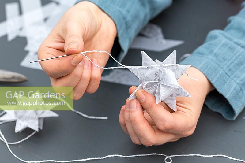 Femme utilisant une aiguille et du fil d'argent pour créer une boucle de suspension sur une décoration en papier.