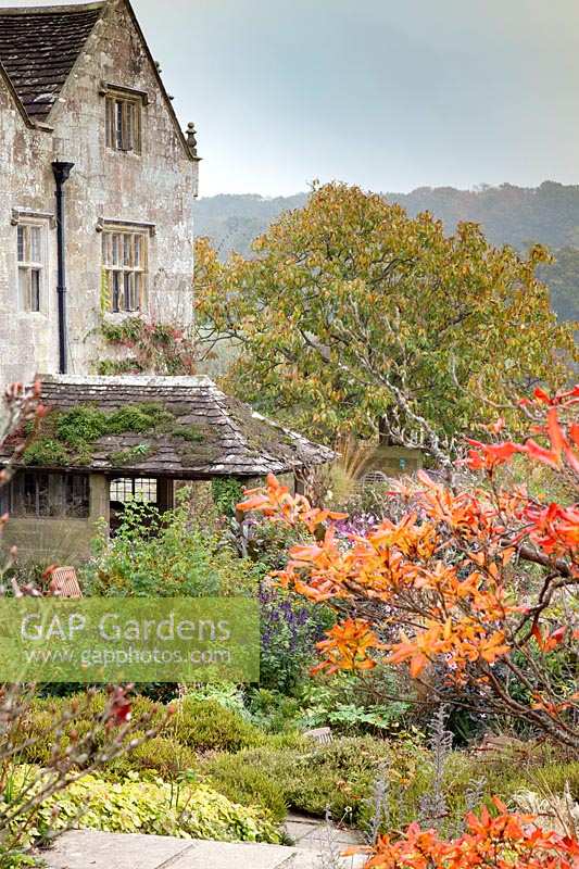 Vue de la maison à travers d'arbustes et d'arbres d'automne dramatiques. Gravetye Manor, Sussex, Royaume-Uni.
